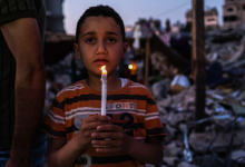 طفل من غزة يحمل شمعة وسط الدمار